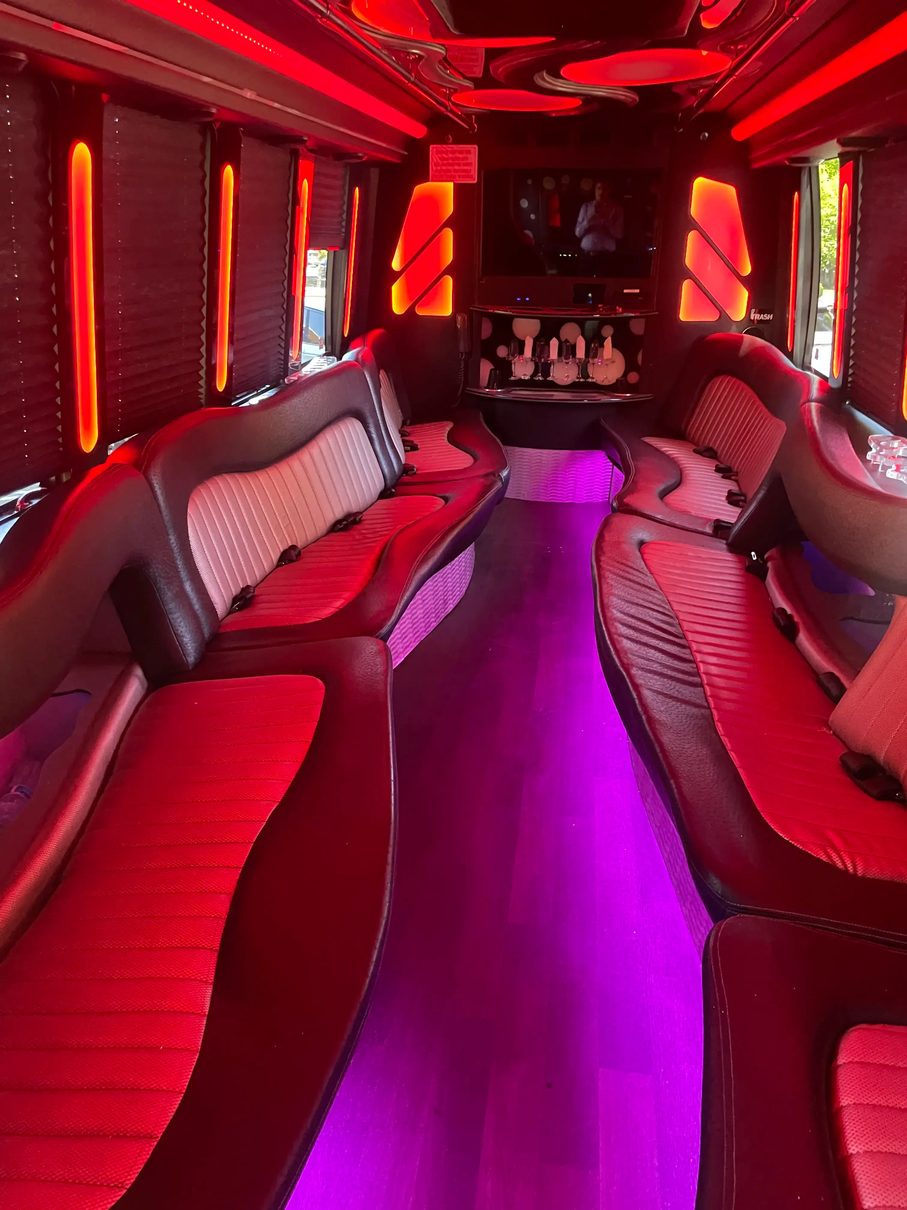 Party bus interior with red leather wraparound seating, LED accent lighting, and a bar